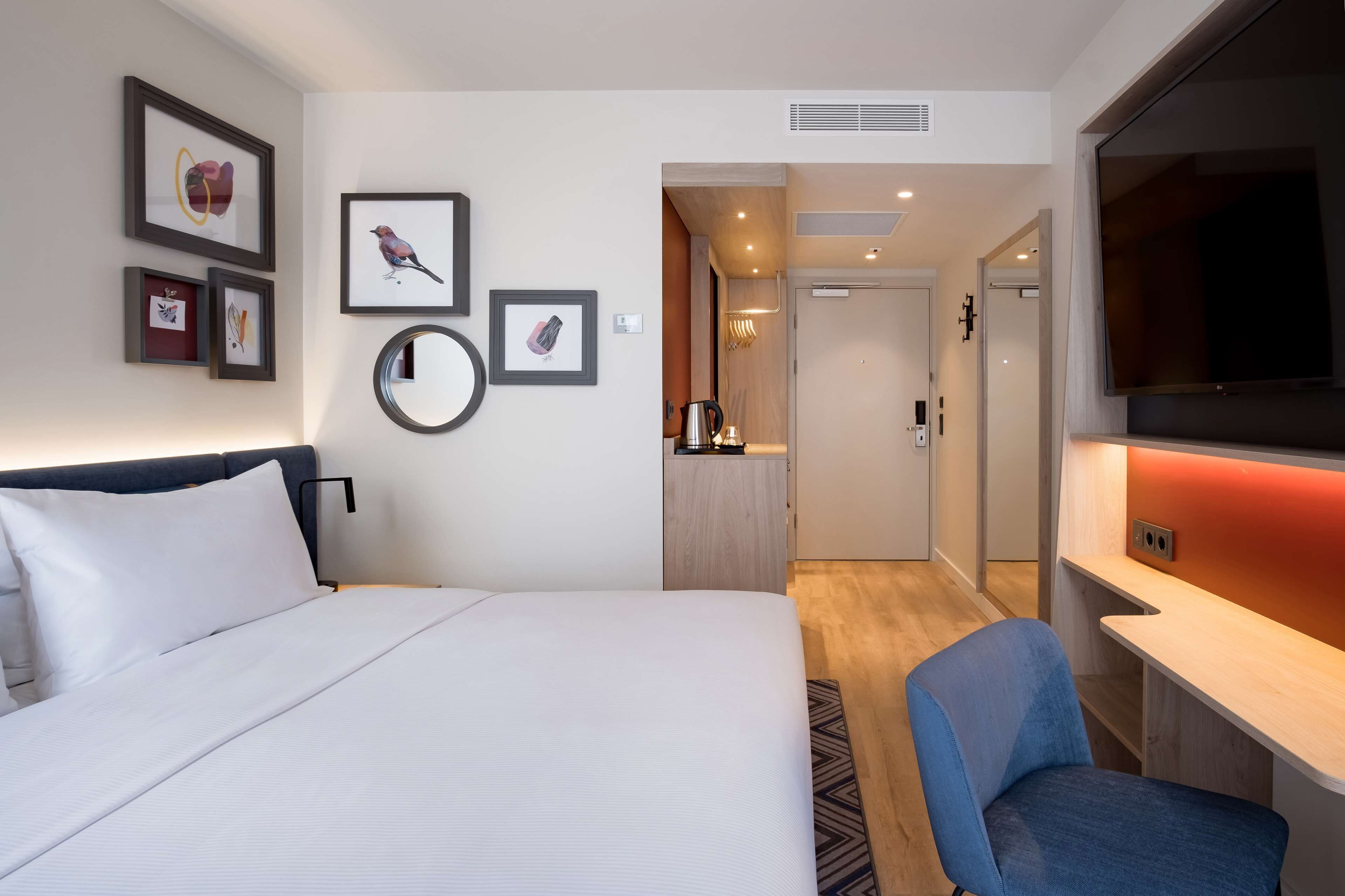 Ein Hotelzimmer mit Bett, Schreibtisch, Stuhl, Fernseher und Bildern an den Wänden.