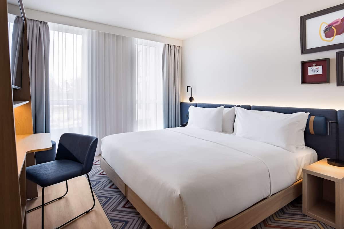 A hotel room with a large bed, a desk, a chair, and a nightstand.