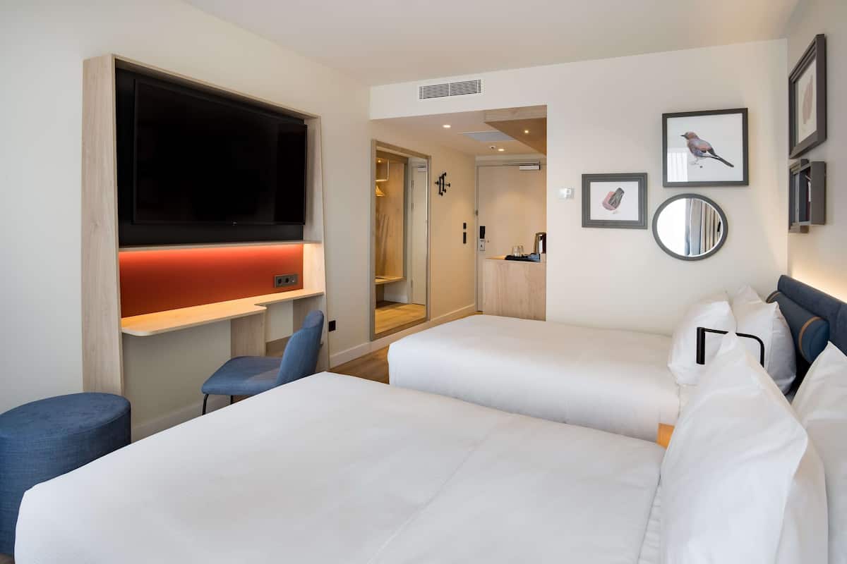 A hotel room with two beds, a TV, a desk, and a mirror.