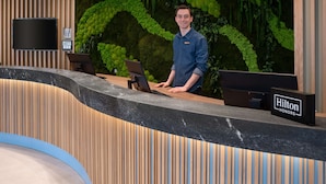 Ein Hotelrezeptionstresen mit modernem Design, einem großen Bildschirm und einer üppigen Grünwand.