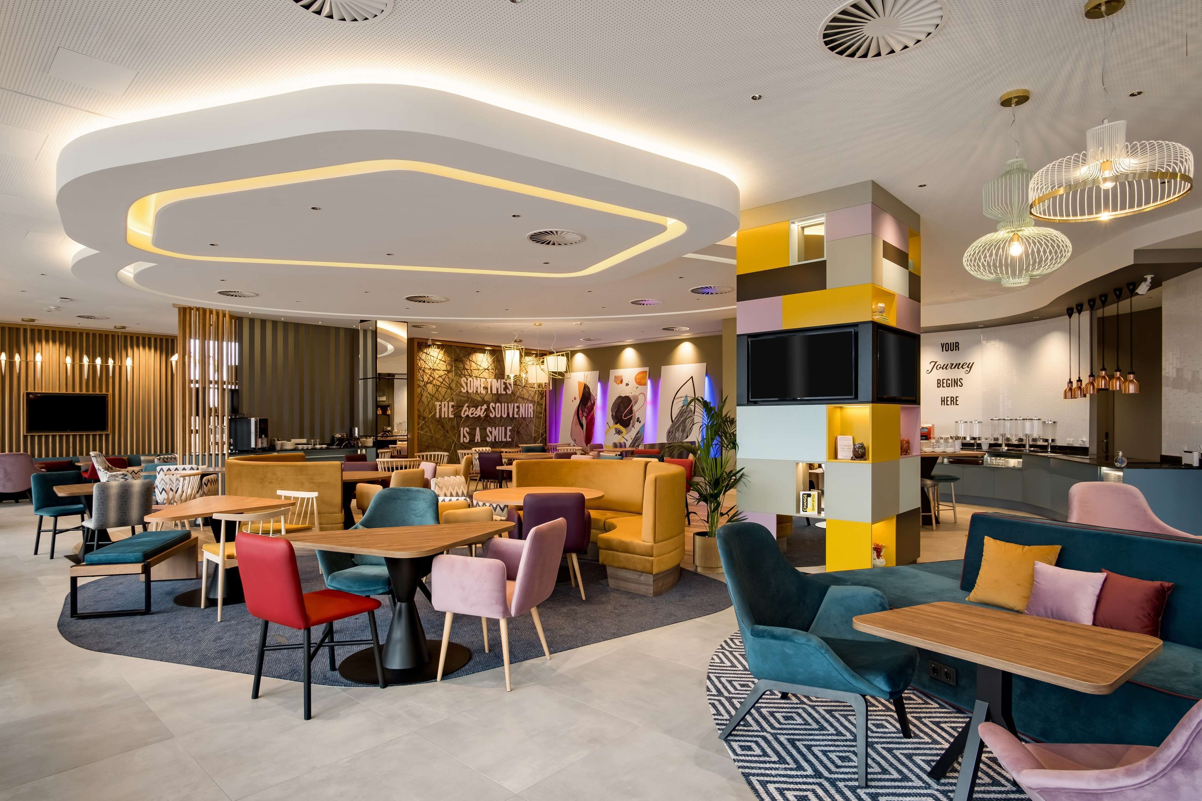 A modern hotel lobby with a central seating area, a bar, and a reception desk.
