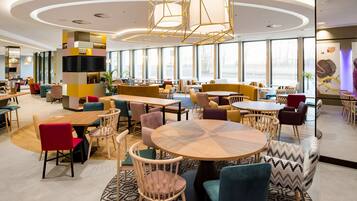 A modern hotel lobby with multiple seating areas, large windows, and contemporary lighting fixtures.