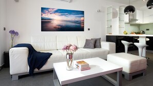 A modern living room with a white sofa, a coffee table, and a painting of a sunset over water. - Sun Spalato Suite (Makarska)