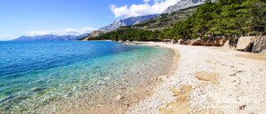 A clear beach with pebbles, a rocky shoreline, and a mountainous backdrop. - Sun Spalato Suite (Makarska)