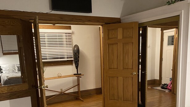 A bedroom with a bed, a wooden wardrobe, a desk with a chair, a television mounted on the wall, and a door leading to another room. - Cheerful Downtown 3 Bedroom home in the historic area of Columbus (Columbus)