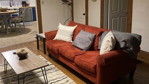 A living room with a red sofa, a coffee table, and a rug. There is a kitchen area visible in the background. - Cheerful Downtown 3 Bedroom home in the historic area of Columbus (Columbus)