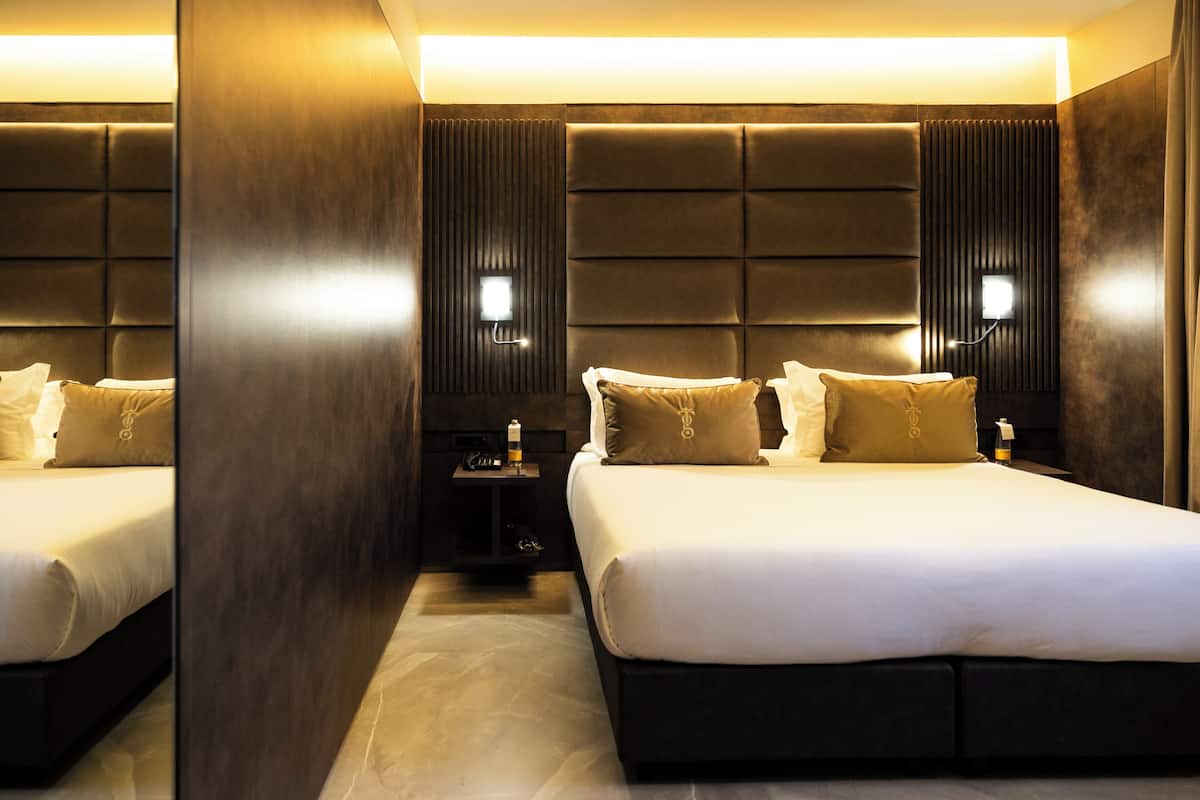 A hotel room with a large bed, two bedside tables, a nightstand, and a wall-mounted light fixture.