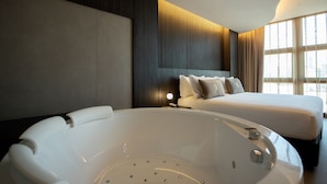 A modern hotel room with a large bed, a white bathtub, and a city view through large windows. - Gold Tower Lifestyle Hotel (Naples)