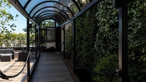 A covered walkway with a glass ceiling, surrounded by greenery and a view of the sky. - Gold Tower Lifestyle Hotel (Naples)