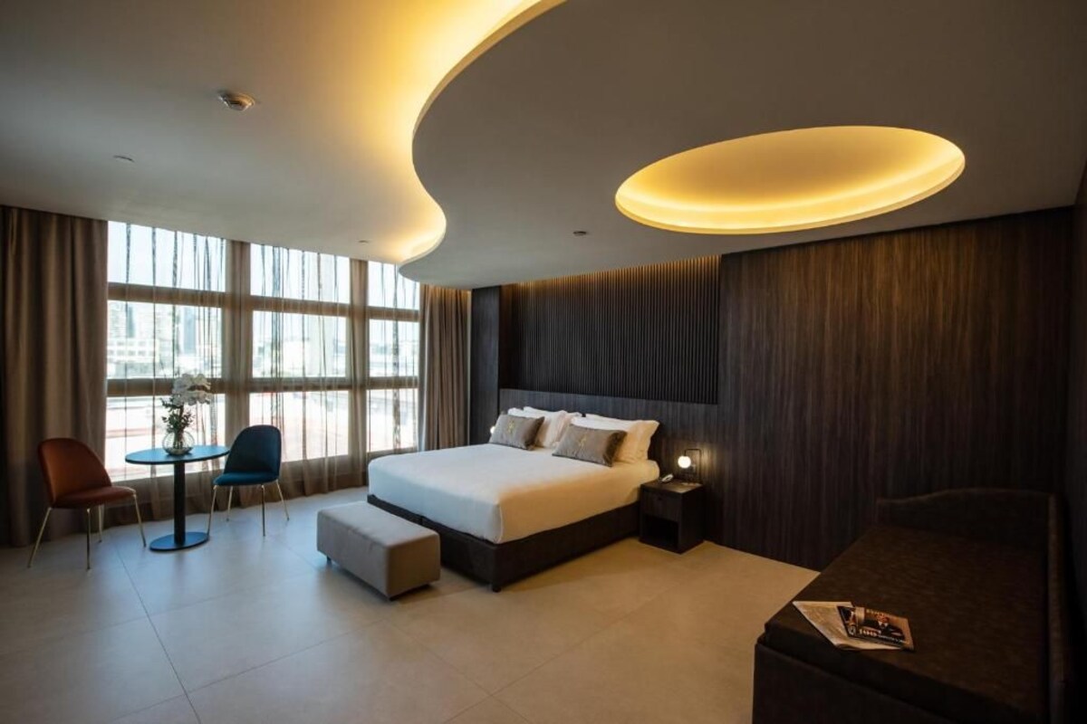 A modern hotel room with a large bed, a desk, a chair, and a small table.