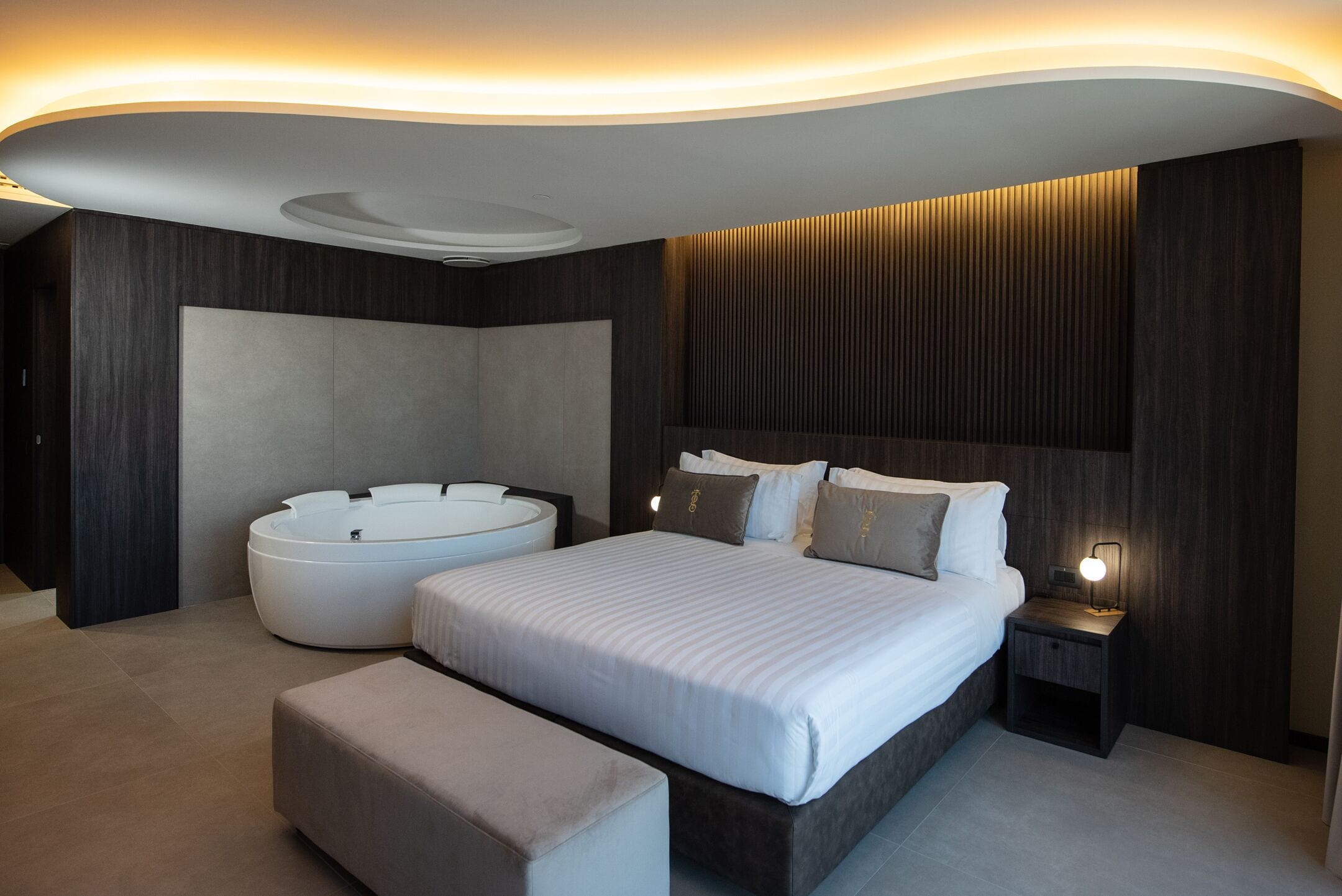 Una camera da letto moderna con un letto grande, una vasca da bagno integrata e un comodino con una lampada.