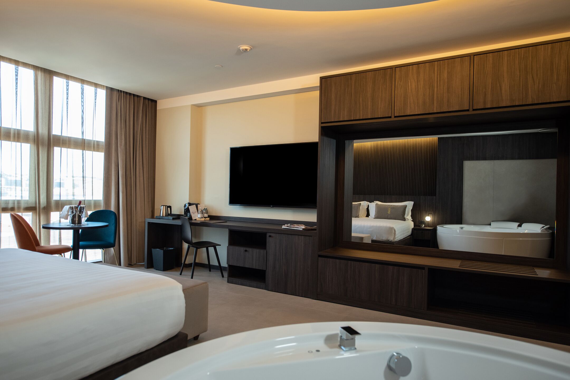 Ein modernes Hotelzimmer mit einem großen Bett, einem Schreibtisch, einem Flachbildfernseher, einem großen Spiegel und einer Badewanne.
