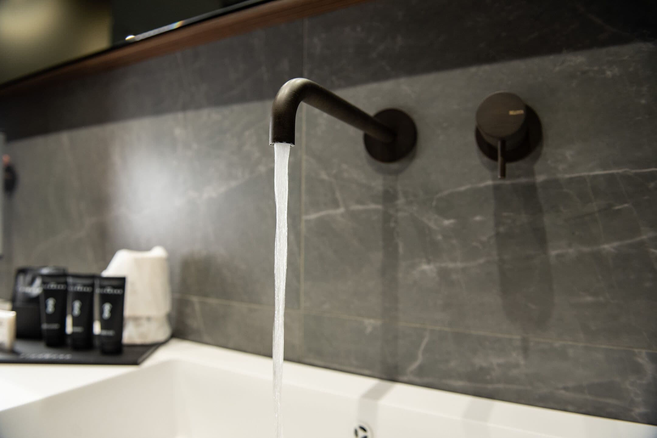 Un bagno con un rubinetto moderno e una parete in marmo.