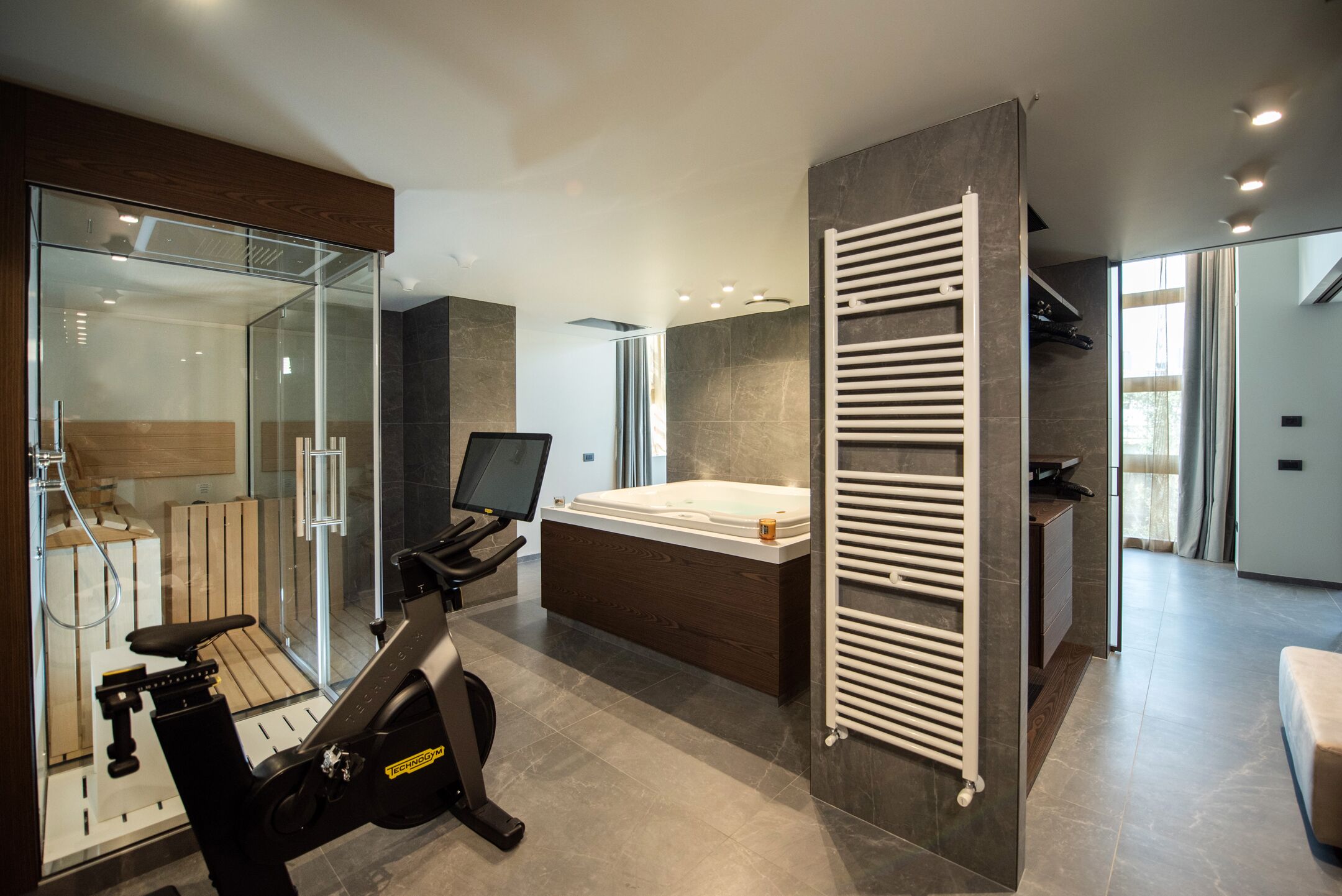 Un baño moderno con cabina de ducha de vidrio, una bicicleta estática empotrada, una bañera grande y un perchero para toallas.