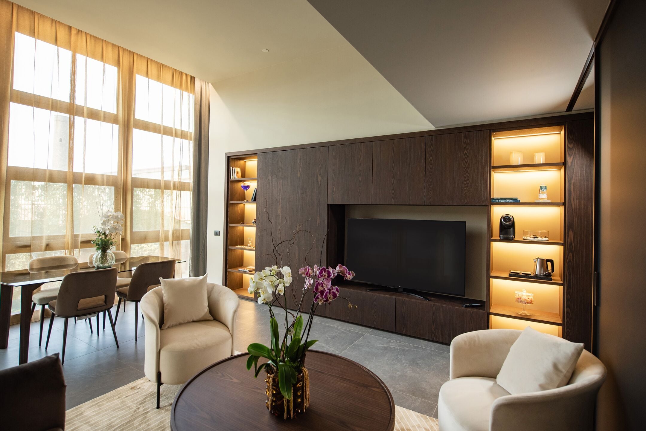 Un salon moderne doté d’un grand téléviseur à écran plat, de sièges confortables et d’un coin repas baigné de lumière naturelle.