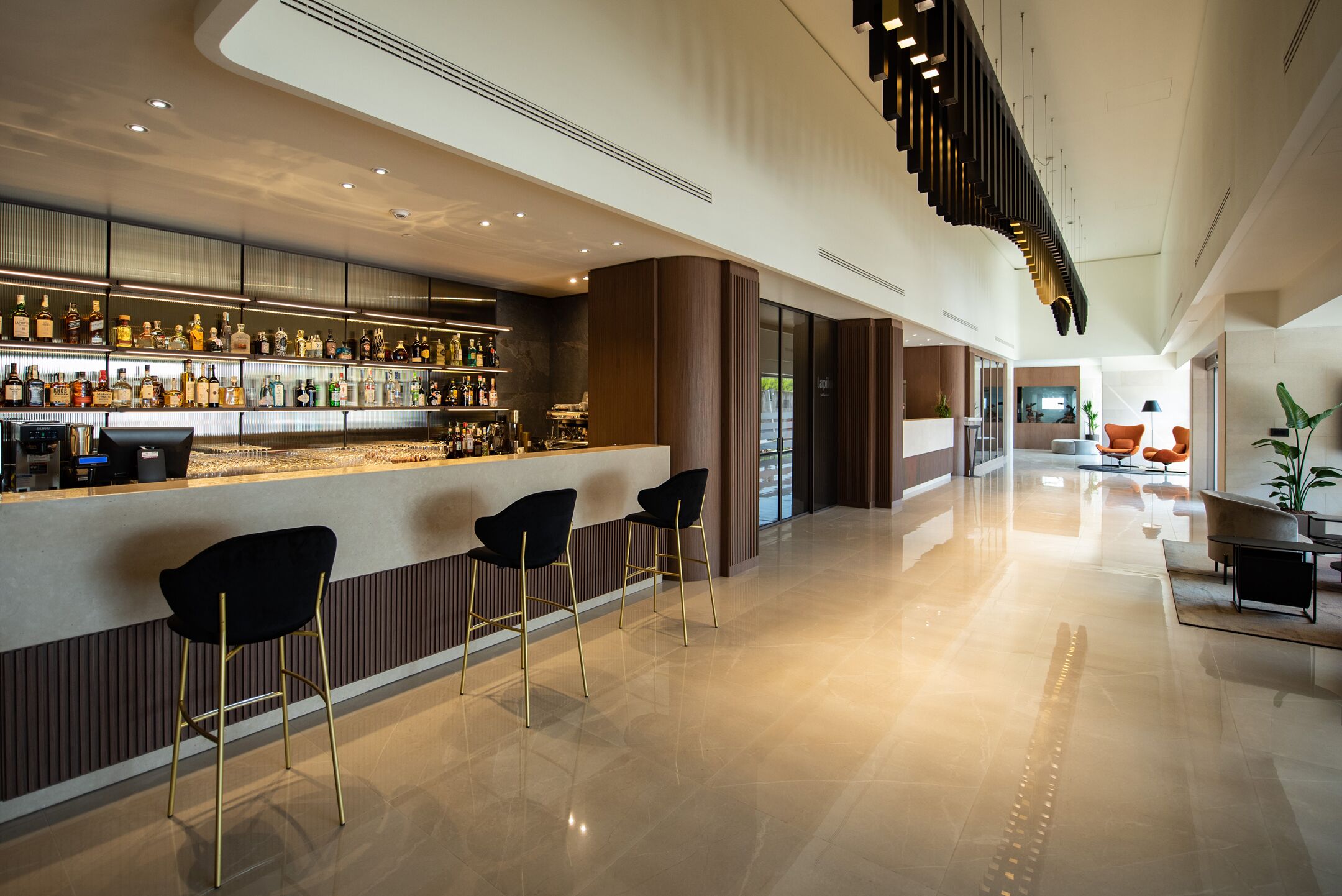 A modern bar area with a polished floor, a long counter with a variety of bottles, and three black bar stools.
