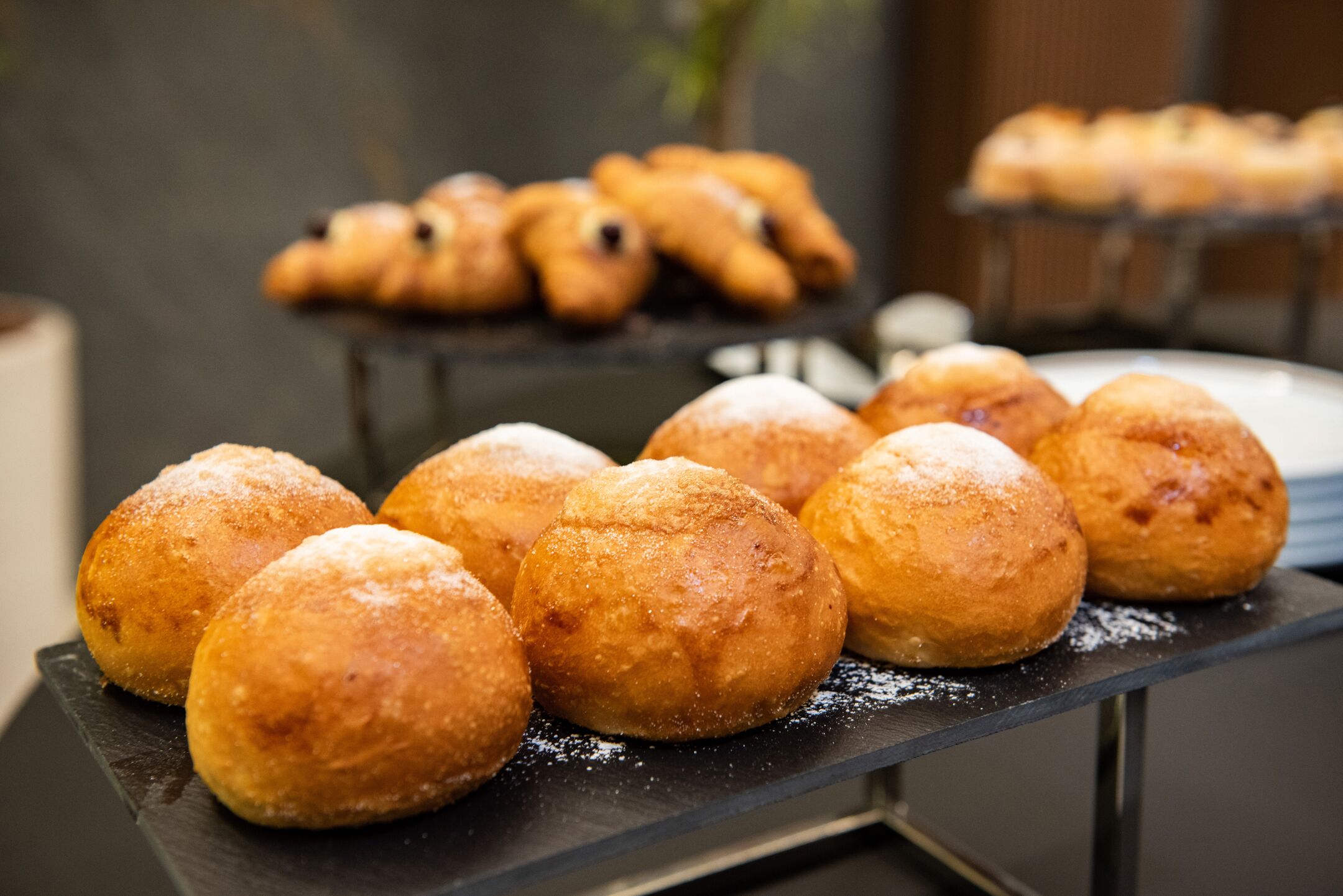 A display of round, golden-brown pastries dusted with powdered sugar, arranged on a black tray.