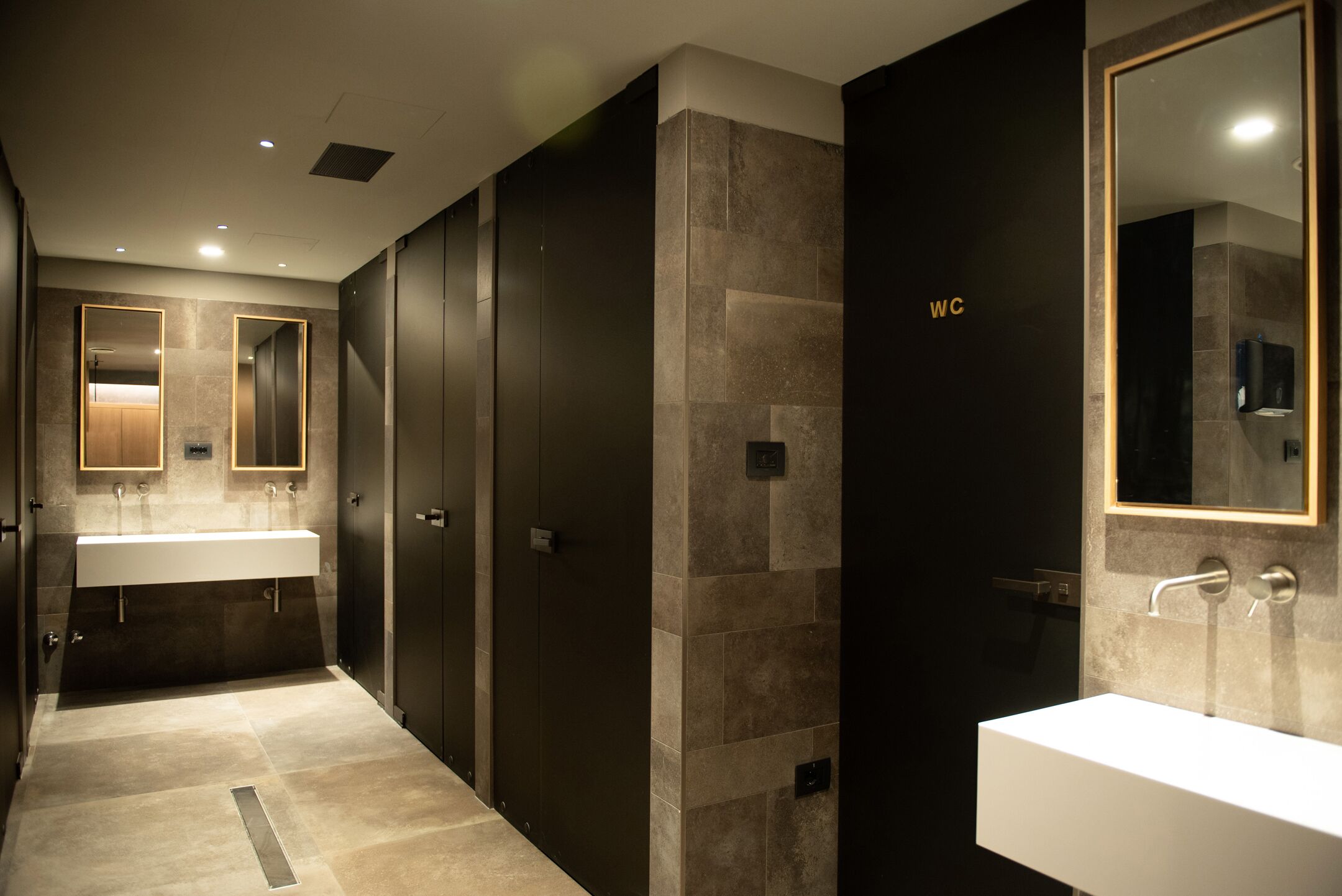 Un bagno moderno con due lavabi, pareti scure e uno specchio grande.
