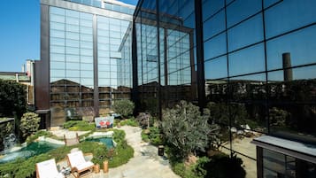Un edificio moderno con facciata in vetro, un cortile curato con piscina e sedie a sdraio.