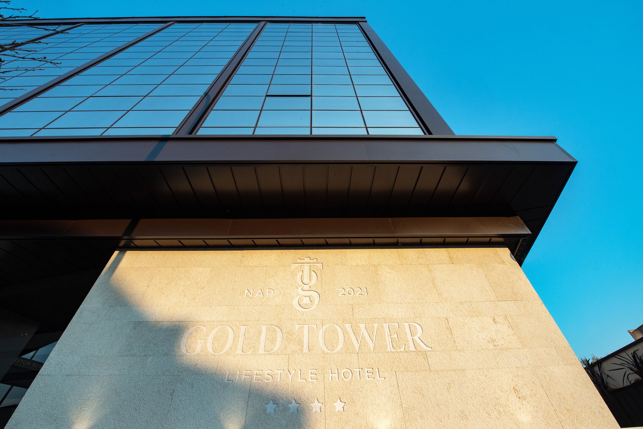 The exterior of the Gold Tower, a modern building with a prominent glass facade and a stone base.