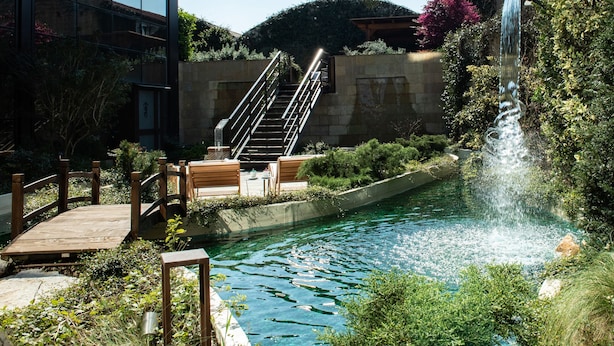 A pool with a waterfall, wooden deck, and stairs leading to a seating area. - Gold Tower Lifestyle Hotel (Naples)