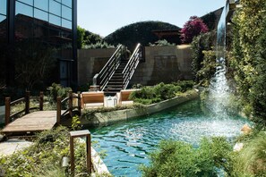 A pool with a waterfall, wooden deck, and stairs leading to a seating area. - Gold Tower Lifestyle Hotel (Naples)