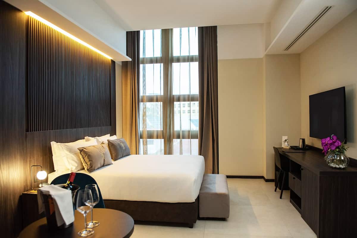 A hotel room with a large bed, a desk, a chair, a TV, and a window with curtains.