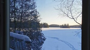 Une vue à travers une fenêtre sur un paysage enneigé, avec des arbres et un ciel dégagé.