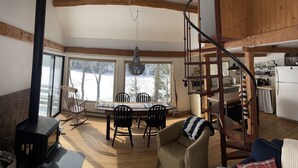Un intérieur de chalet chaleureux comprenant un coin repas, un poêle à bois, un escalier en colimaçon et une cuisine.