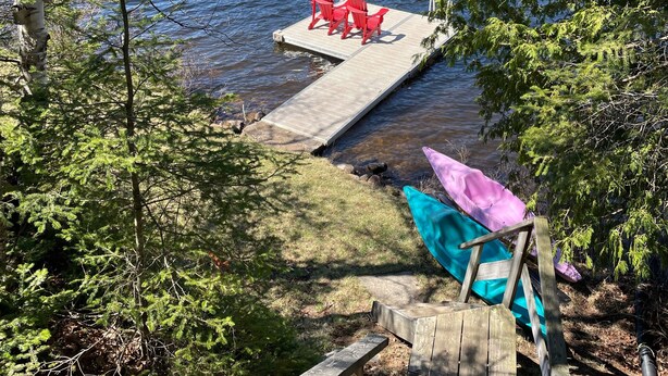 Une jetée en bois s’avançant dans un lac, entouré d’arbres, avec des chaises rouges et un espace abrité.