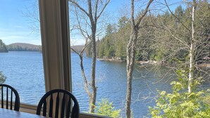 Une table à manger avec des chaises, donnant sur un lac grâce à de grandes fenêtres.