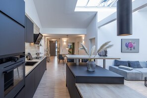 Een moderne keuken met donkere kastjes, een centraal eiland en een zithoek met een bank en tafel.