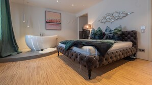 A bedroom with a large bed, a bathtub, and a wall-mounted artwork.