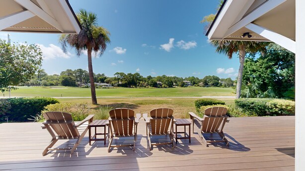 Een terras met houten stoelen en tafels, met uitzicht op een golfbaan.