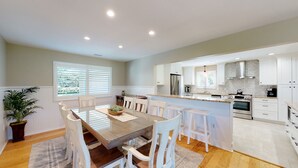 Een moderne keuken met witte kasten, een centraal eiland en een eethoek met een houten tafel en witte stoelen.