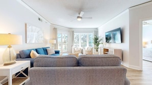 Un salon moderne avec un canapé gris, une table d’appoint blanche et un ventilateur de plafond.