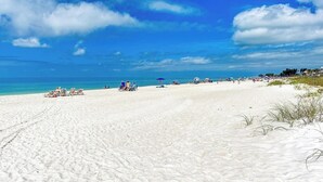 A wide sandy beach with clear blue water and a few umbrellas.