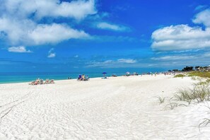 A wide sandy beach with clear blue water and a few umbrellas.