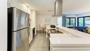 Een moderne keuken met roestvrijstalen apparatuur, een eethoek met een tafel en stoelen, en een uitzicht op de omgeving door grote ramen.