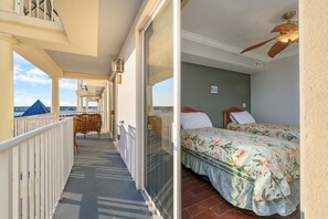 Un balcone con vista sul mare, un letto con lenzuola a motivi floreali e una ventola a soffitto.