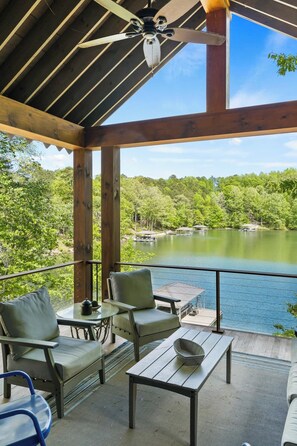 A covered outdoor area with a view of a lake, wooden deck, and seating.
