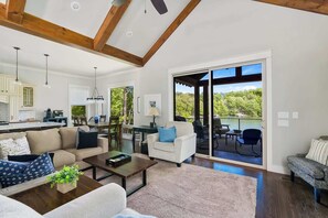 A spacious living room with a large sliding glass door leading to an outdoor deck, a kitchen with white cabinetry, and a dining area with a table and chairs.