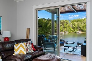 A living room with a brown leather sofa, a red lamp, and a view of a lake through a sliding glass door.