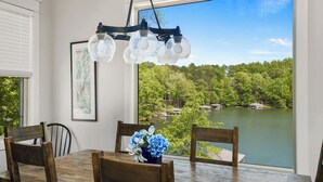 Un comedor con mesa y sillas de madera, una araña y vista a un lago con barcos.