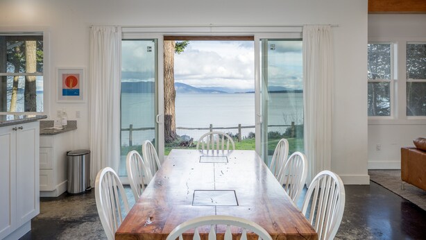 A dining area with a wooden table and white chairs, large windows with a view of the sea, and a view of the sky. - Orcas Island, Peapod Cottages with Barn #290B (Orcas Island)
