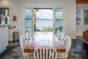 A dining area with a wooden table and white chairs, large windows with a view of the sea, and a view of the sky.