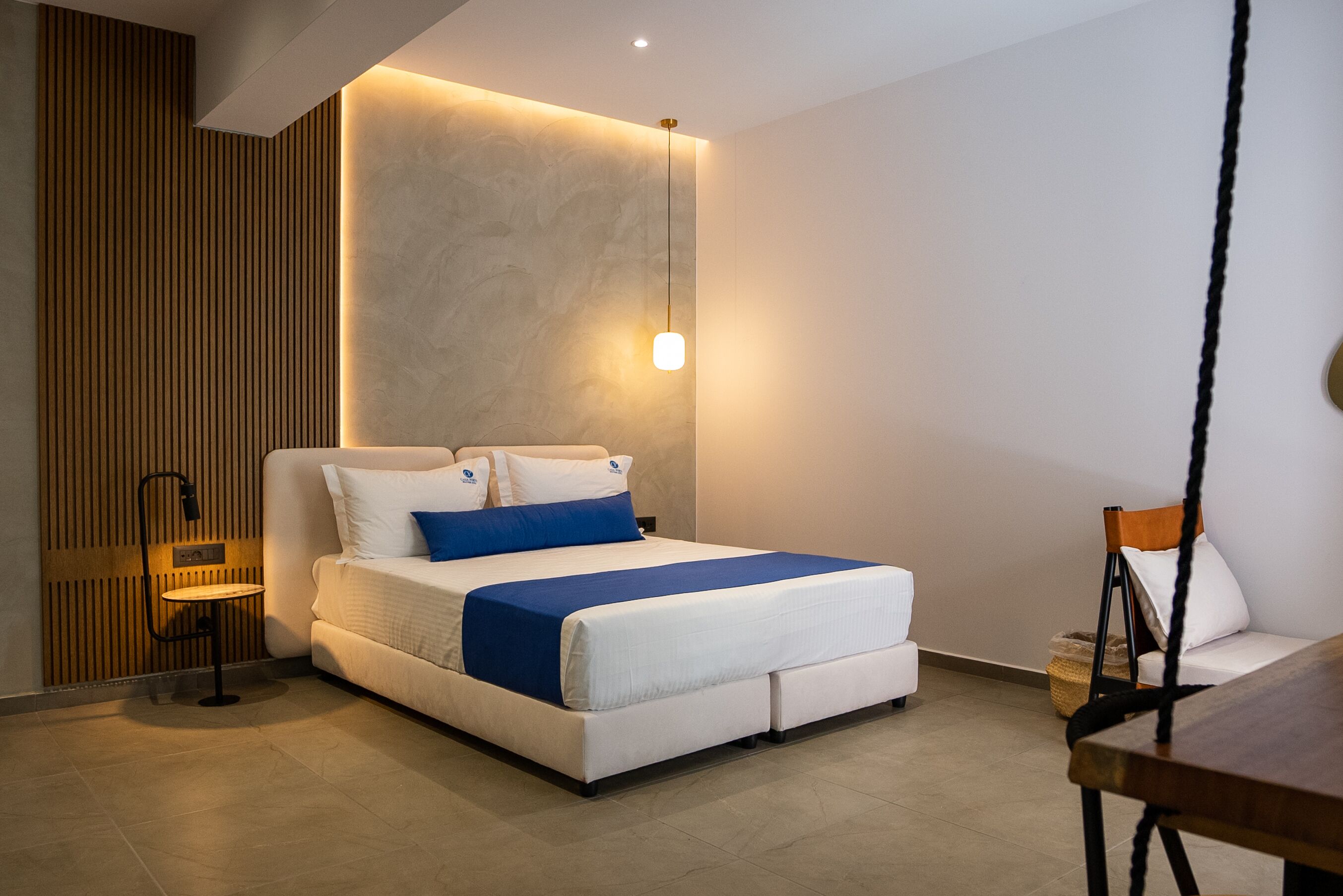 Una camera d'albergo moderna con un letto grande, un tavolino, una sedia e una lampada a sospensione.