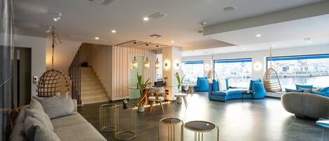 A modern hotel lobby with a staircase, seating areas, and large windows overlooking a cityscape.