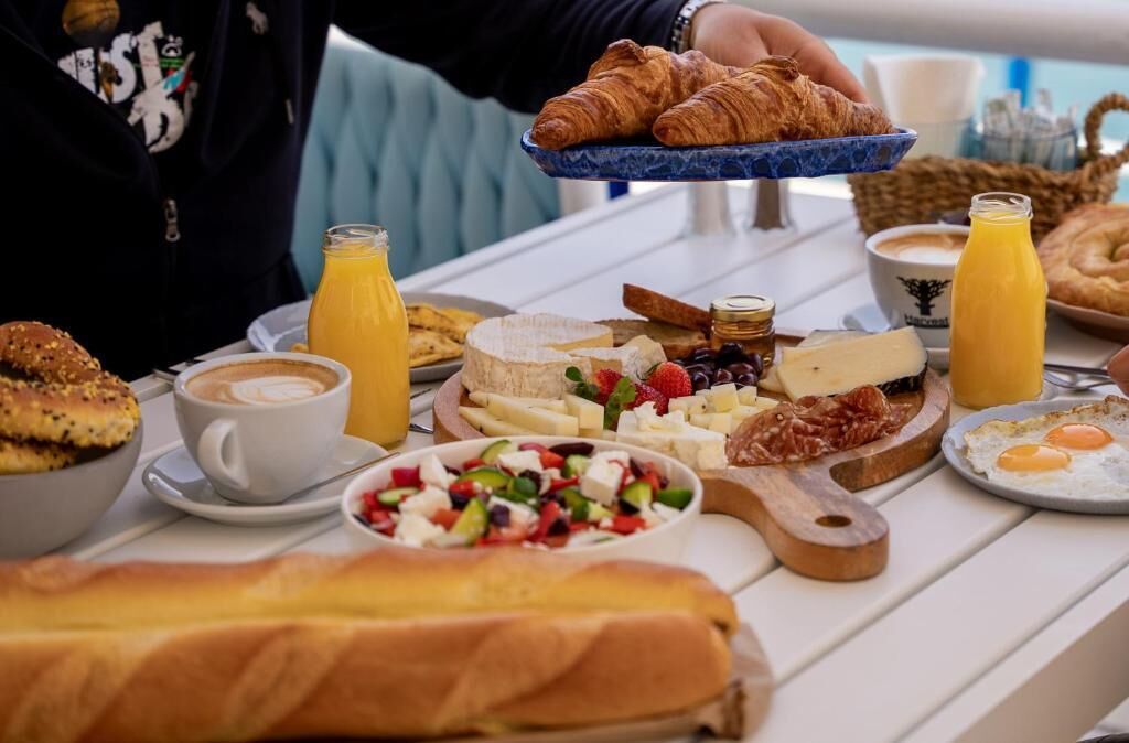 Una mesa de desayuno con cruasanes, queso, frutas y café.