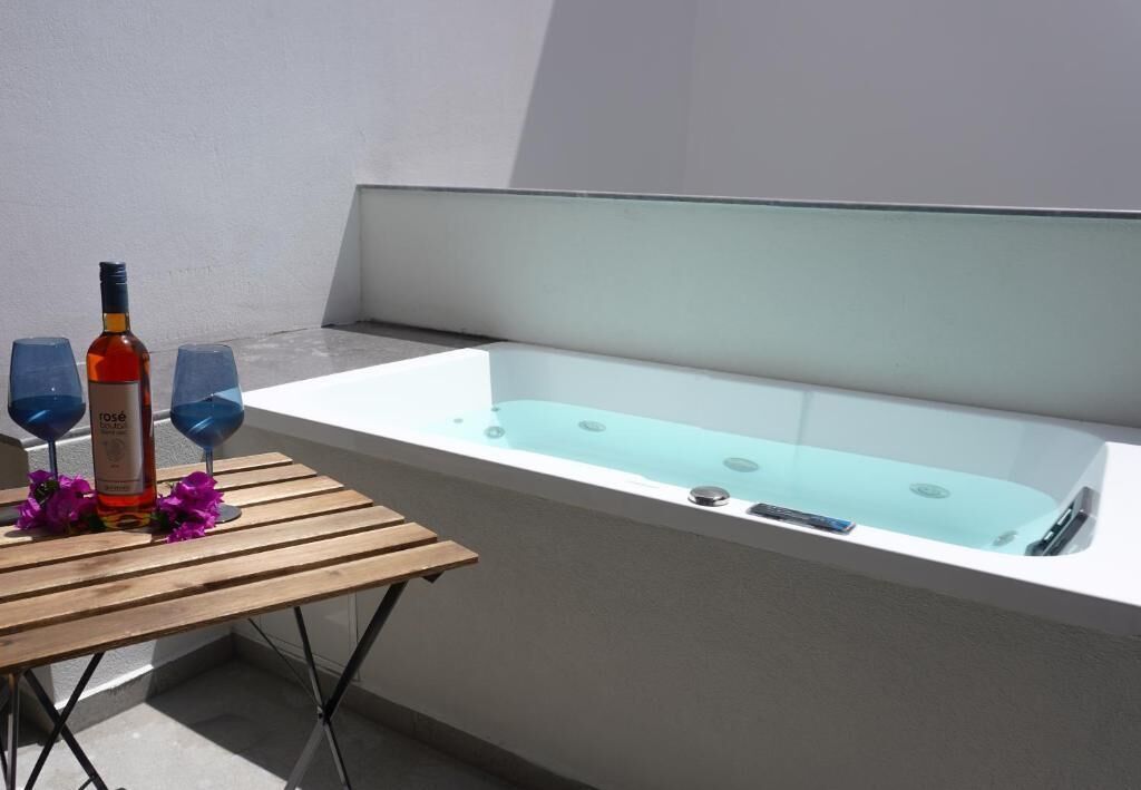 A spa area with a bathtub, two wine glasses, and a bottle of lotion on a wooden table.